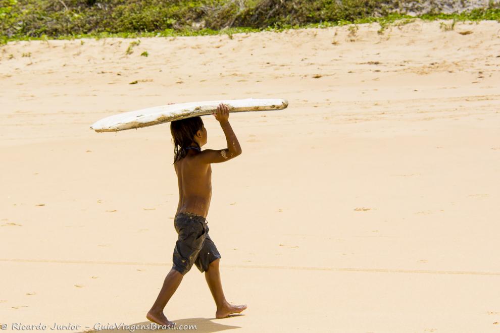 Imagem de um menino levando prancha na cabeça na Praia de Caraiva.
